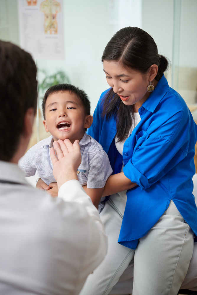 ENT doctor checking young boy's mouth and throat with mother