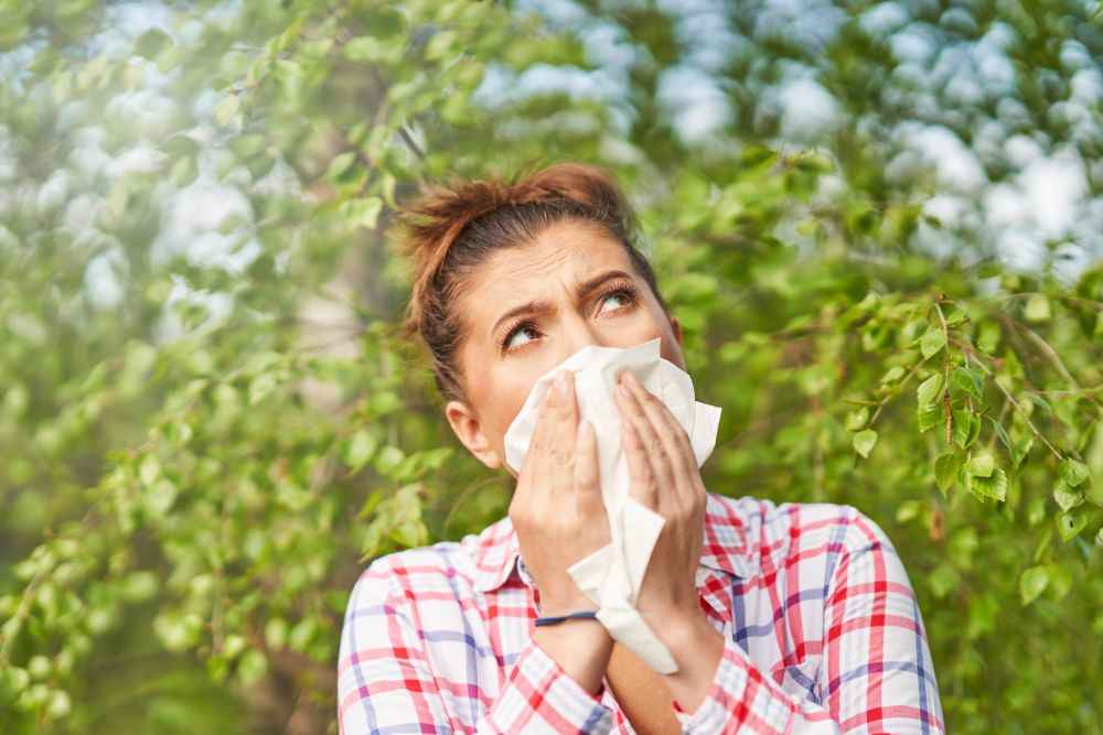 Woman sneezing into a tissue while outside and experiencing allergies